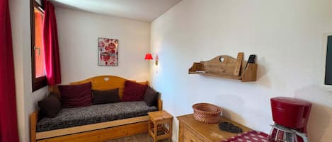 A cozy room with a wooden bed, a small wooden table, a red coffee maker, and a wall-mounted shelf with a lamp.