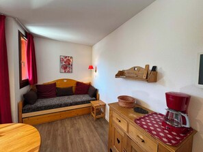 Habitació acollidora amb un llit de fusta, una taula de fusta petita, una cafetera vermella i una prateleira penjada amb una làmpada.
