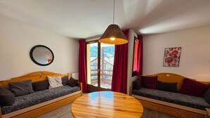 A room with two wooden sofas, a round wooden table, a hanging light fixture, a mirror, and a window with red curtains.