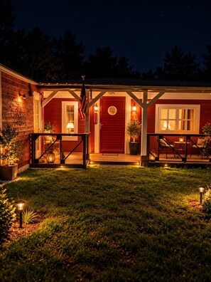 A red wooden building with a porch, a flag, and outdoor lighting. - Love Room - Jacuzzi privatif - Romantique (Pissos)