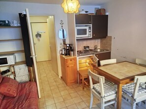 A compact kitchen with a microwave, stove, and sink. There is a dining table with chairs and a small cabinet above the stove. - Magnifique studio au pied des montagnes (Prapoutel)