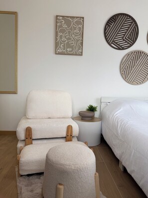 Ein Schlafzimmer mit einem Bett, einem Sessel, einem kleinen Tisch mit einer Pflanze und Wanddekoration.