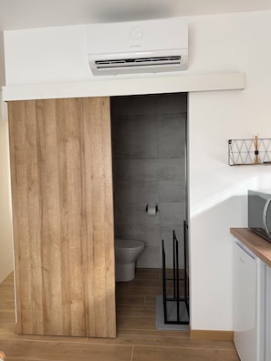 A modern bathroom with a wooden partition, a toilet, a bidet, and a Bosch air conditioner.