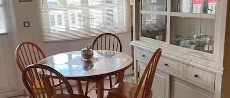 Un comedor con una mesa redonda y sillas de madera, una ventana con persianas y un armario blanco con puertas de cristal.