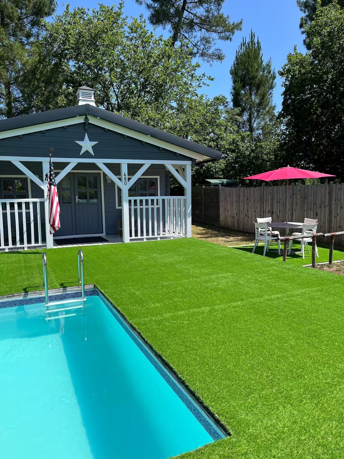 Ein Garten mit Swimmingpool, überdachter Terrasse und Holzzaun.