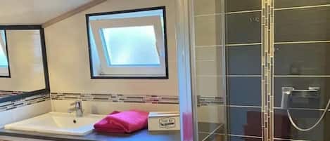 A compact bathroom with a washing machine, a sink, and a glass-enclosed shower.