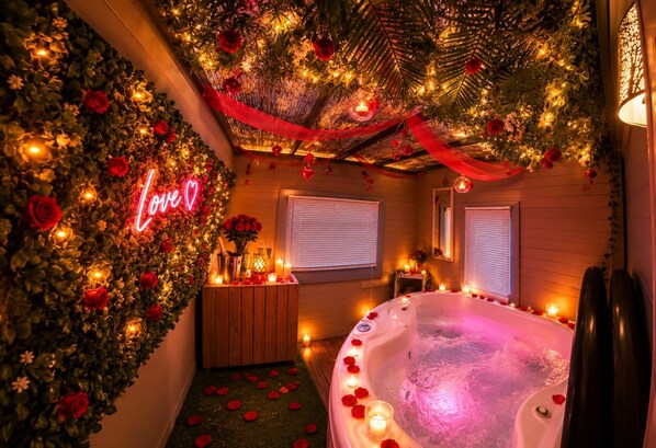A romantic setting with a jacuzzi, floral decorations, and a neon 'Love' sign.