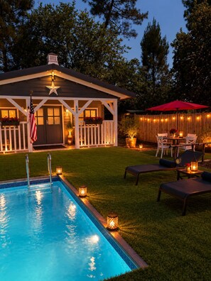 A backyard with a swimming pool, a covered patio with outdoor furniture, and a wooden fence.