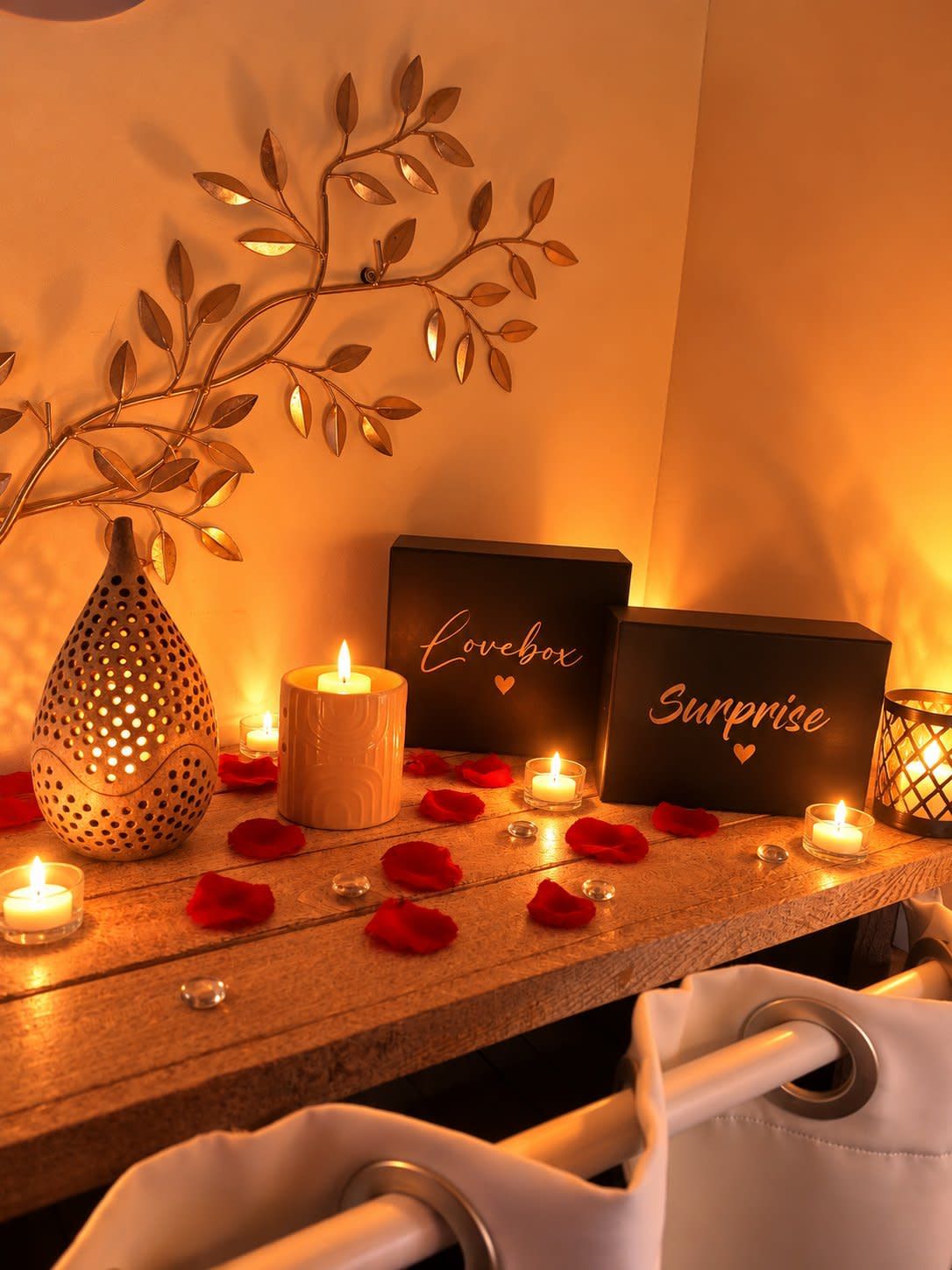 Une ambiance chaleureuse, avec des bougies, une branche décorative et deux panneaux indiquant les mots « Lovebox » et « Surprise » sur une surface en bois.