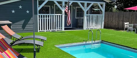 A backyard with a swimming pool, lounge chairs, and a house with a star decoration.