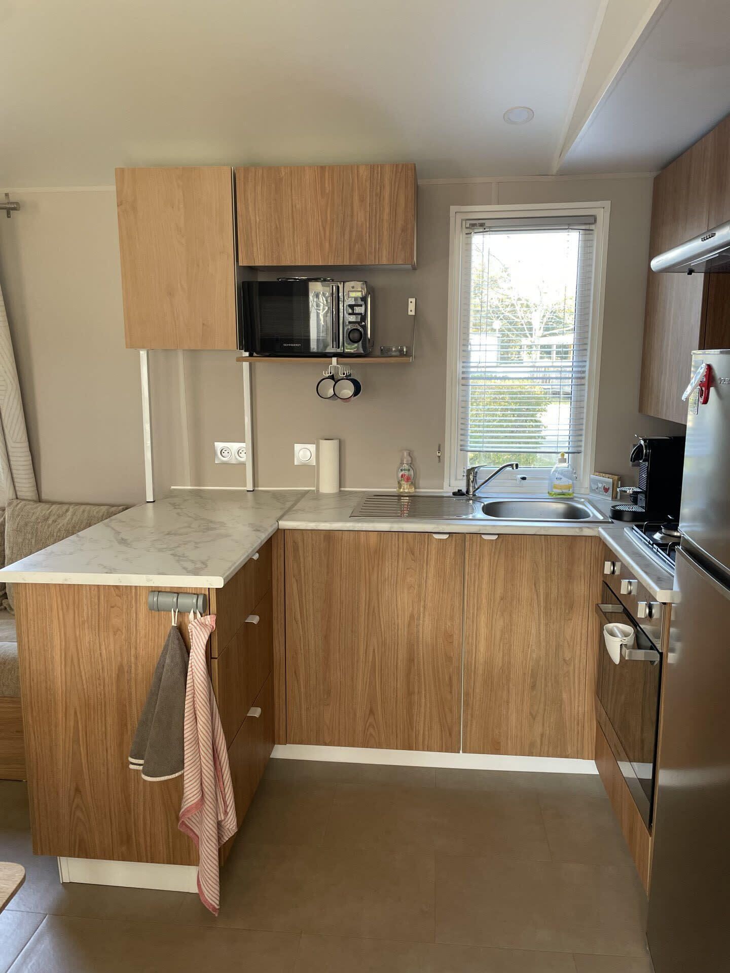 Una cocina compacta con armarios de madera, microondas integrado, pileta y refrigerador de acero inoxidable.