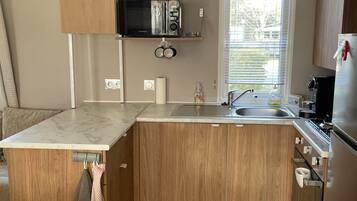 Una cocina compacta con armarios de madera, microondas integrado, pileta y refrigerador de acero inoxidable.