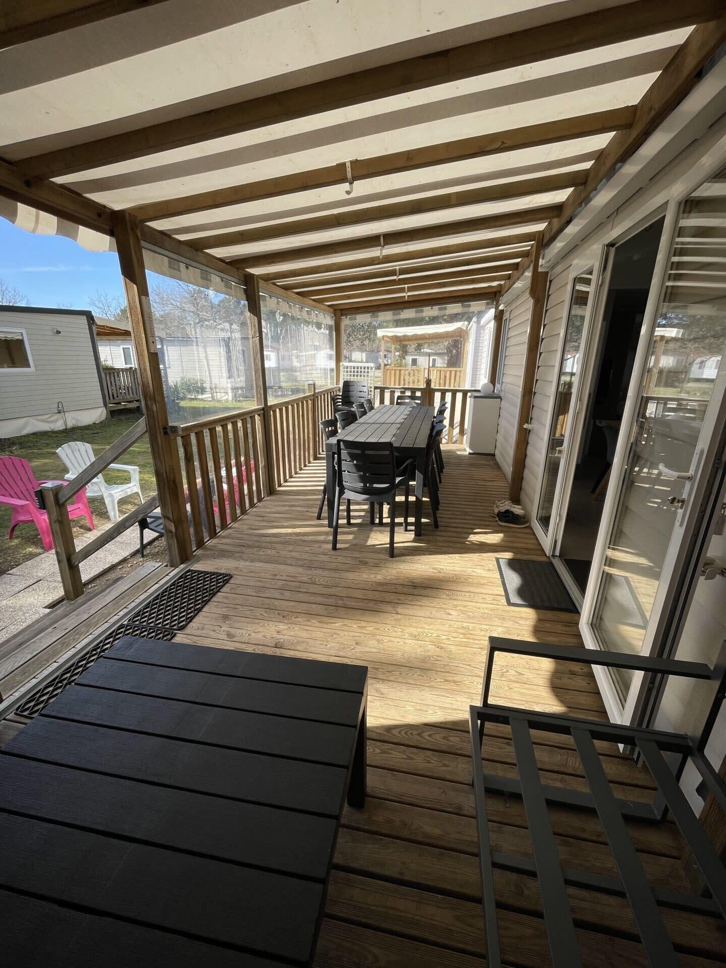Una terraza cubierta al aire libre con mesa y sillas, barandilla de madera y un ventanal corredero.