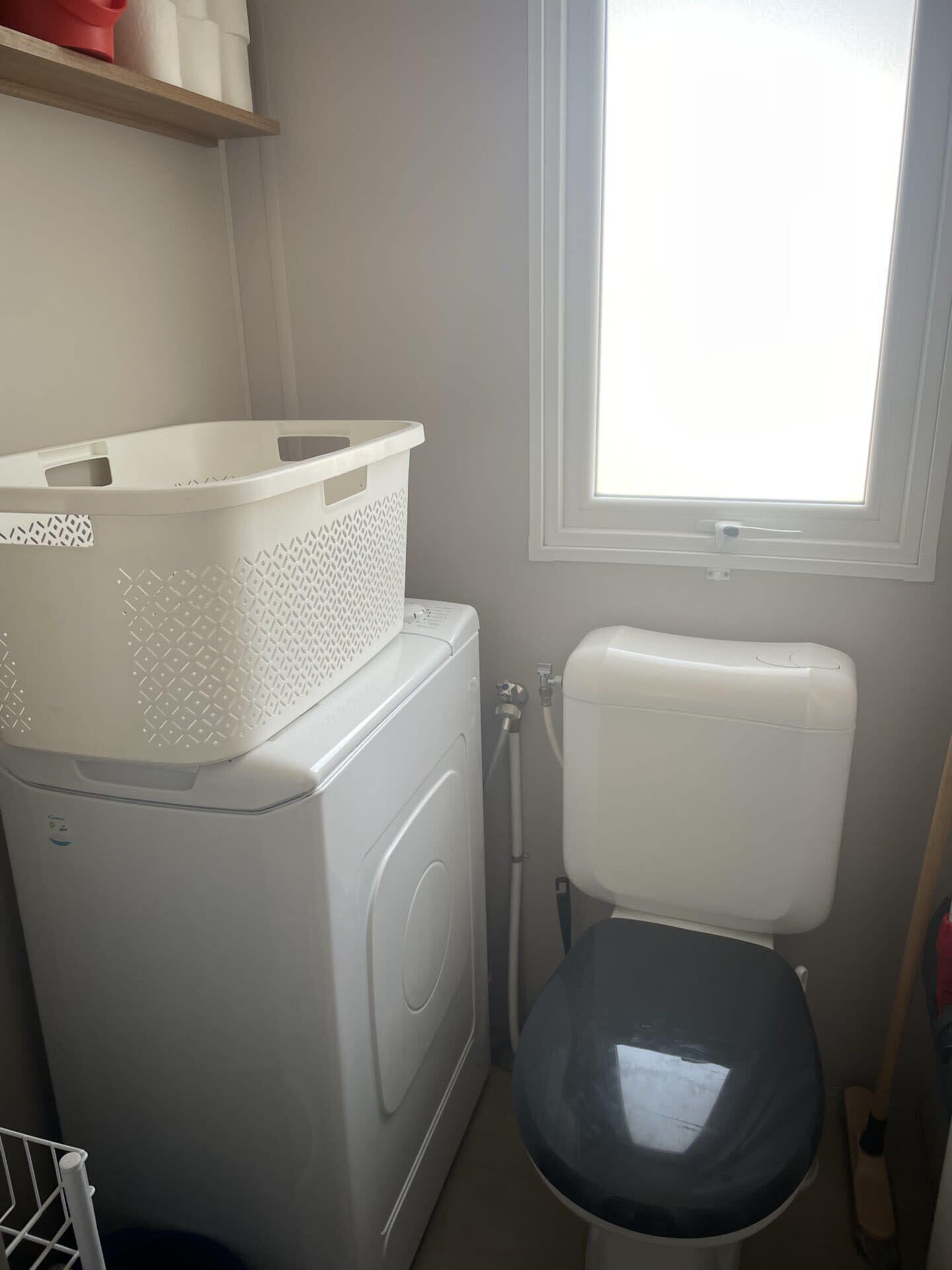 A compact laundry area with a washing machine, a white basket, and a toilet.