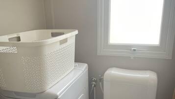 A compact laundry area with a washing machine, a white basket, and a toilet.
