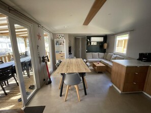 Ein geräumiger Wohnbereich mit einem Holzesstisch, grauen Stühlen, einer Couch und einer Küchenzeile mit Schränken und einer Kaffeemaschine.