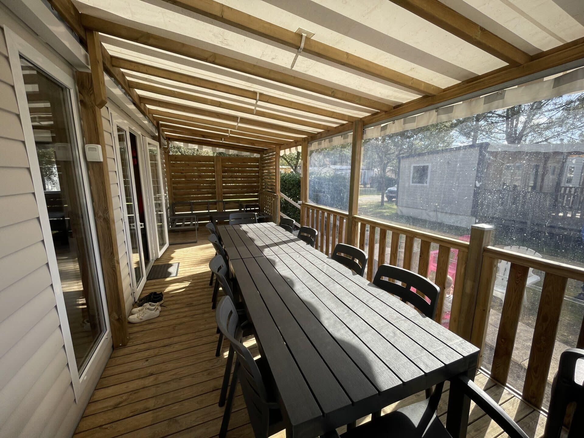 A covered outdoor deck with a wooden table and chairs, a sliding glass door, and a view of a residential area.