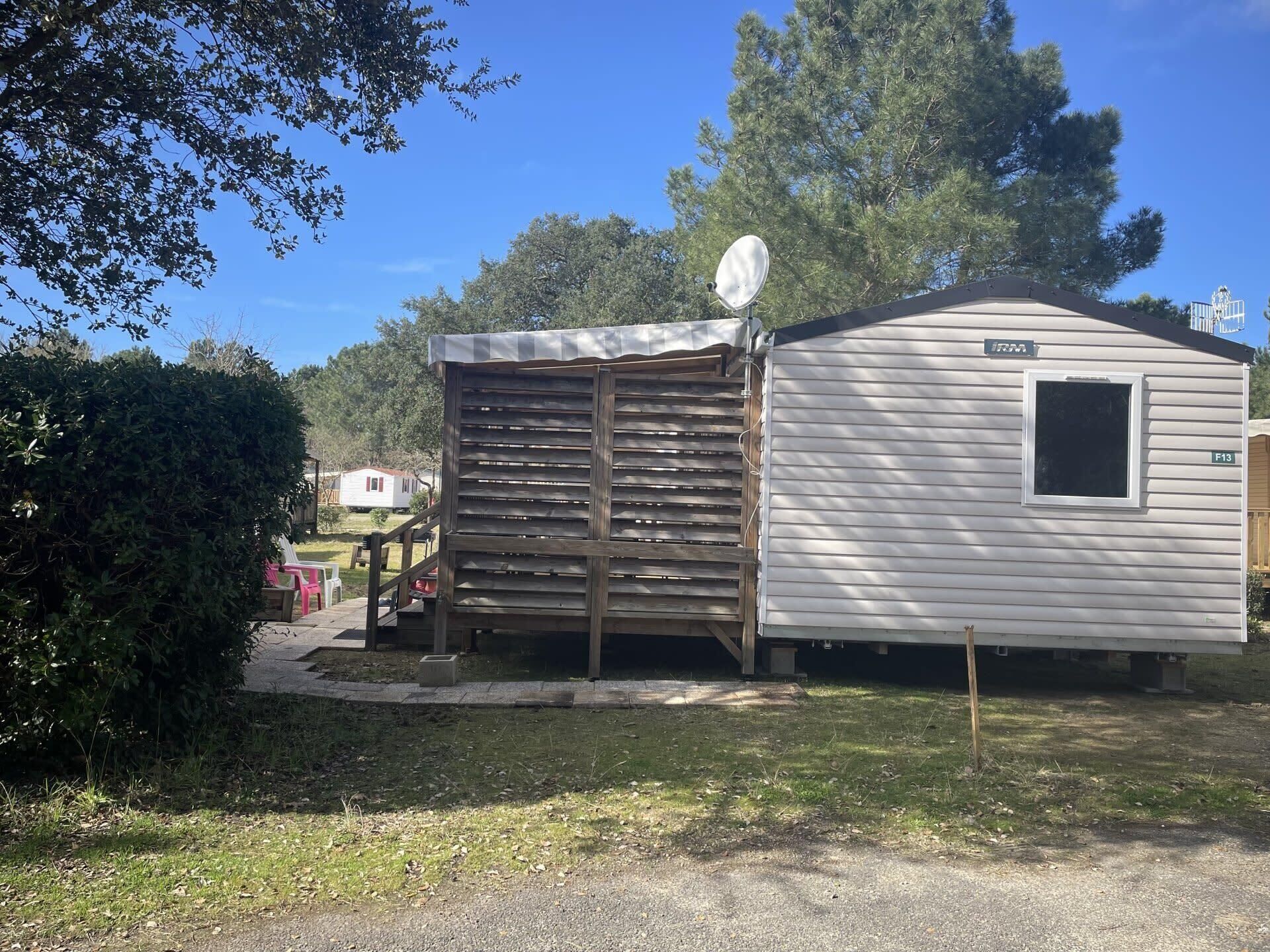 A mobile home with a satellite dish, a small porch, and a paved driveway.