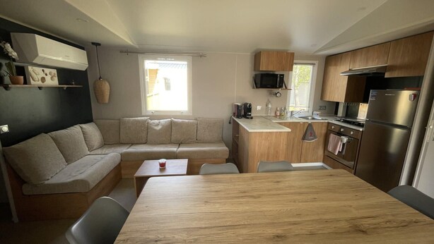 A compact kitchen with a wooden table, a built-in bench, and a microwave. - Mobil-home 3 chambres 1 sdb (Mimizan)
