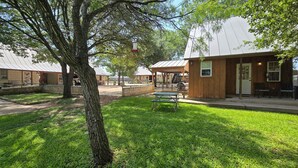 A park with picnic tables, a covered seating area, and a building with a wooden facade. - Luckenbach Gruene Cottages (New Braunfels)