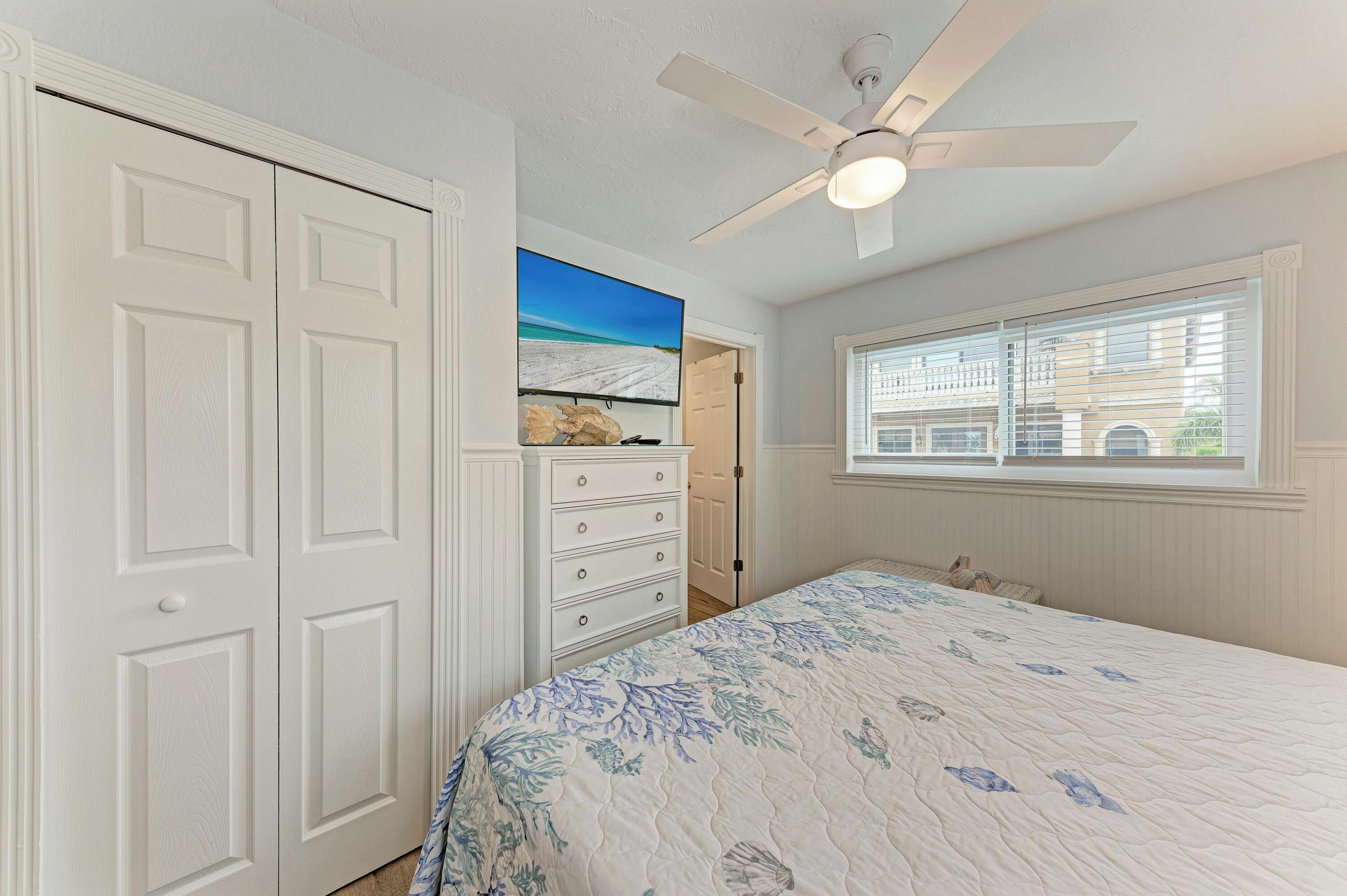 A bedroom with a bed, a dresser, a ceiling fan, and a window with blinds.