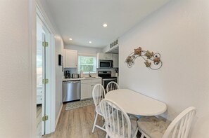 A compact kitchen with white cabinets, a microwave, a stove, and a dining area with a white table and chairs. - Seagrass Shores Unit 3 (Bradenton Beach)