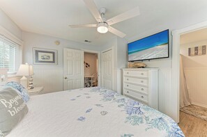Quarto com cama, ventilador de teto, televisão e porta que dá para outro cômodo.