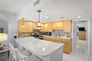 A modern kitchen with a central island, wooden cabinets, stainless steel appliances, and a tiled backsplash. - 🌅 Birdsong #26 — Just Steps to the Sand from this Treasure Island Delite (Treasure Island)
