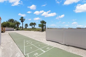 Una cancha de juego de shuffleboard con los números del 1 al 10, rodeada por una zona arenosa con palmeras y una valla blanca.