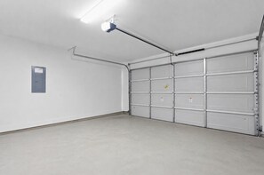 Eine saubere, leere Garage mit einer einzelnen Leuchtstofflampe, einer Metalttür und einem kleinen Stromverteiler am Wand.