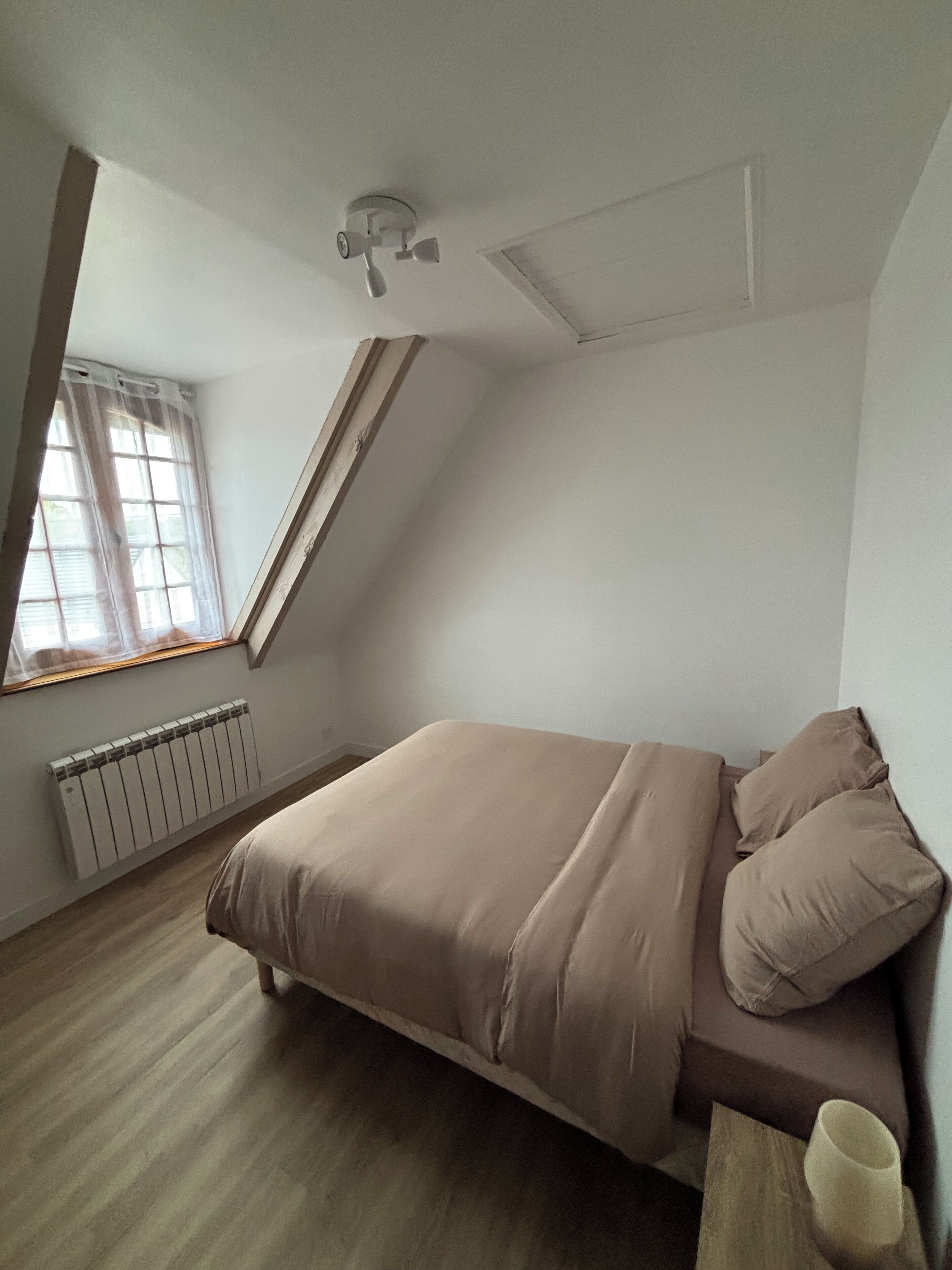 Een slaapkamer met een bed, een radiator, een raam met gordijnen en een plafondventilator.