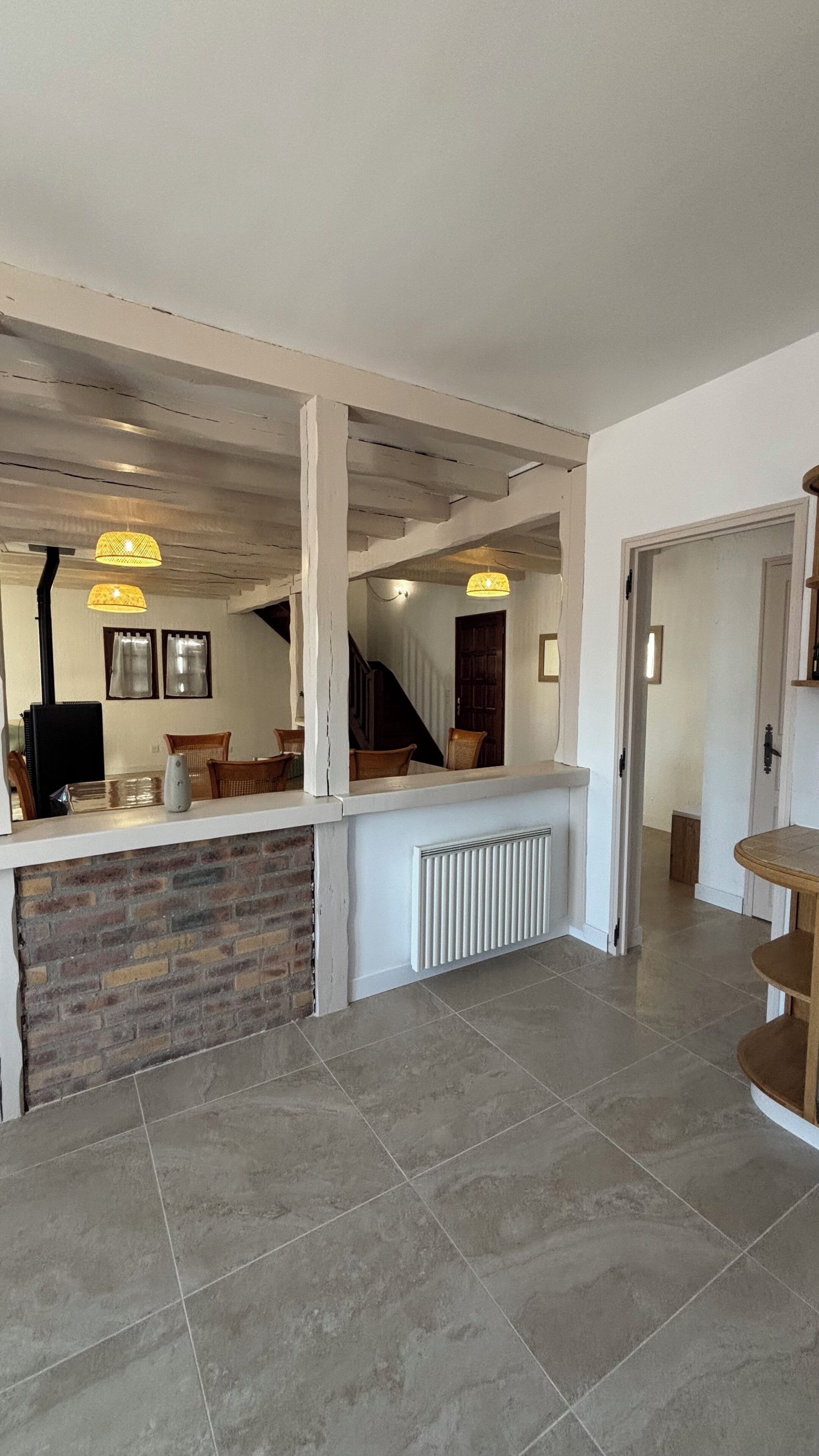 Une pièce spacieuse avec un mur d’accent en briques, un plafond blanc avec des poutres apparentes, un banc intégré et un escalier menant à un autre niveau.