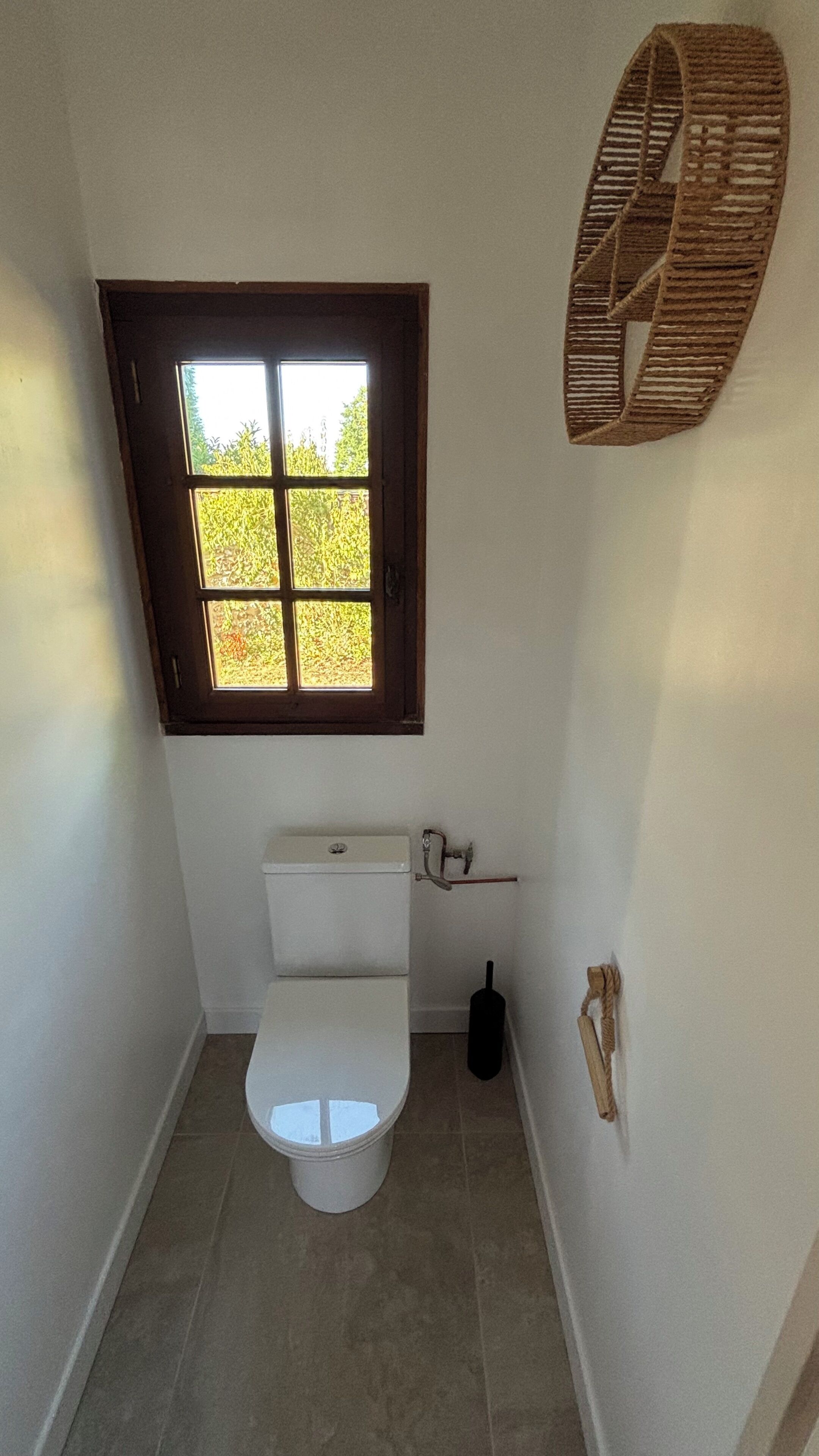 Une petite salle de bain avec des toilettes, une fenêtre et un porte-serviettes.