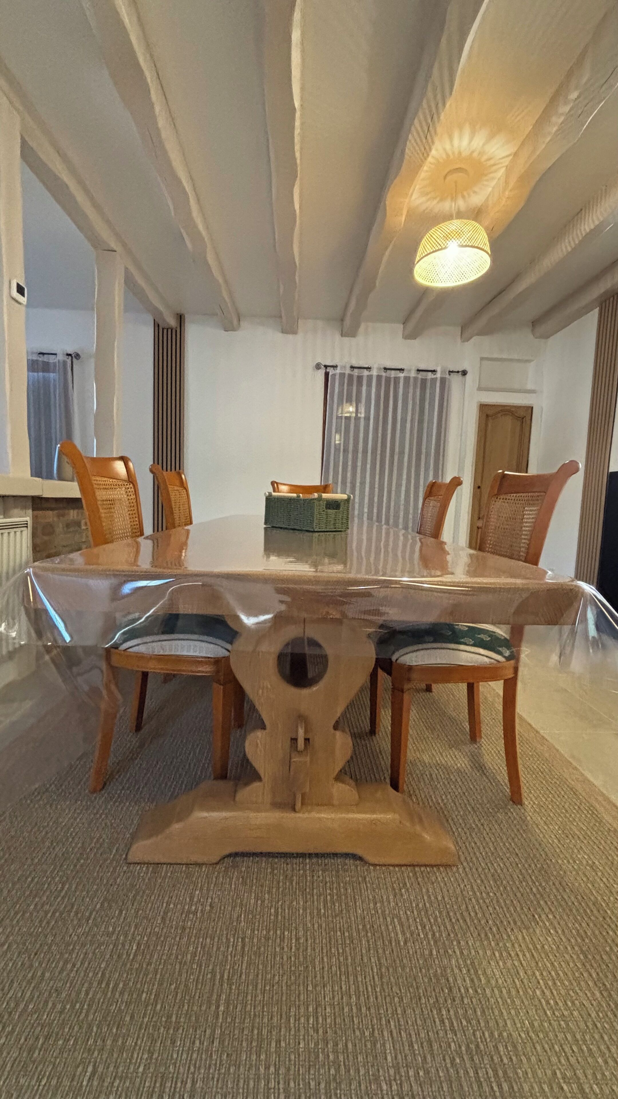 Un coin repas comprenant une table à plateau en verre, des chaises en bois, un panier en osier et un luminaire suspendu au plafond.