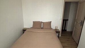 Een slaapkamer met een groot bed, een nachtkastje, een lamp en een deur naar een andere kamer.