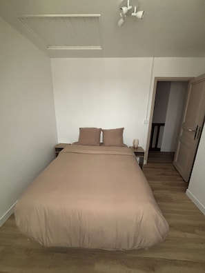 Um quarto com uma cama grande, uma mesinha de cabeceira, um abajur e uma porta que dá para outro espaço.