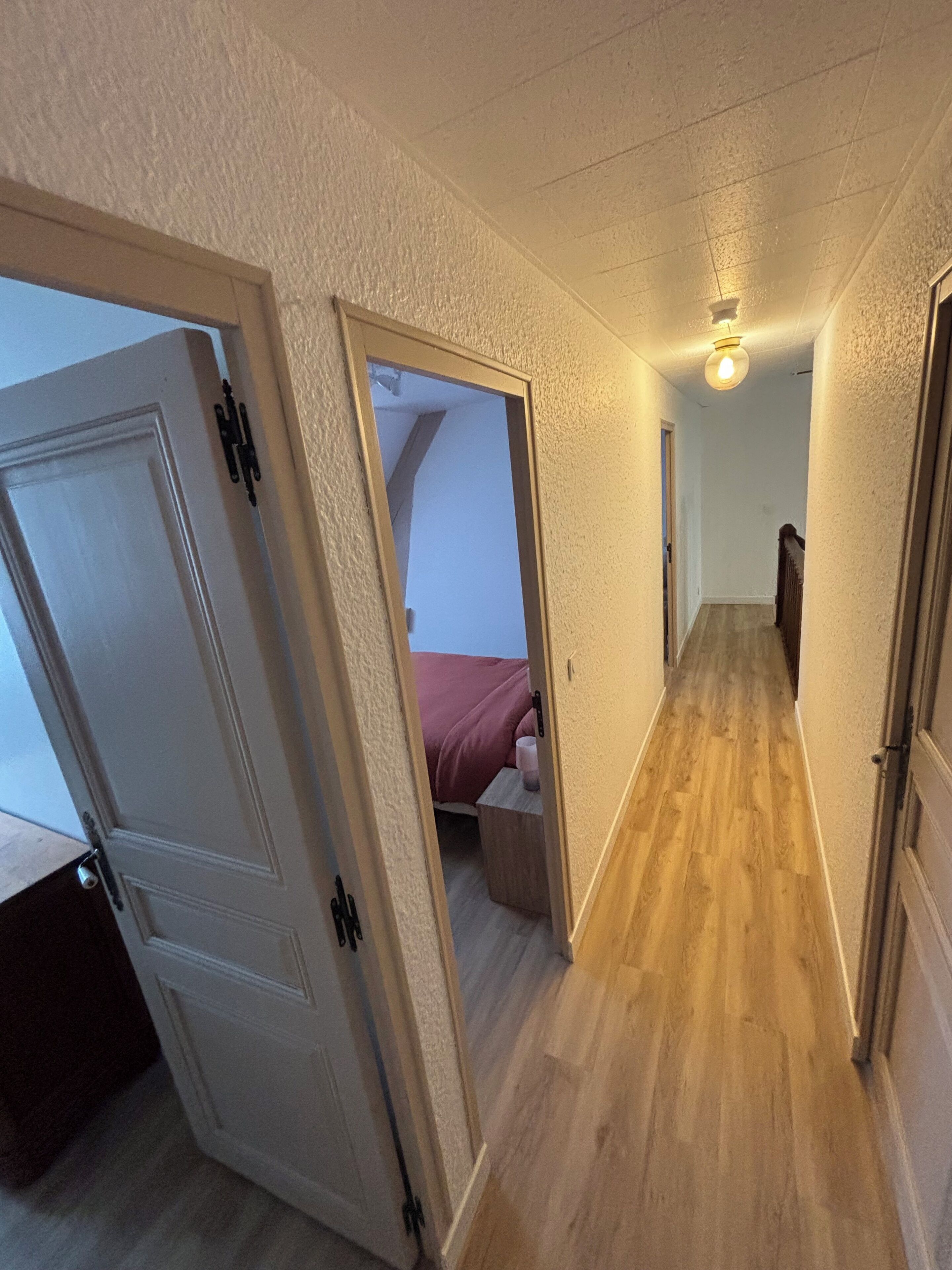 A narrow hallway with wooden flooring, white walls, and a ceiling light fixture.