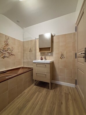 Une salle de bain avec un plancher en bois, des carreaux de couleur beige, un lavabo avec un miroir et un meuble de rangement.