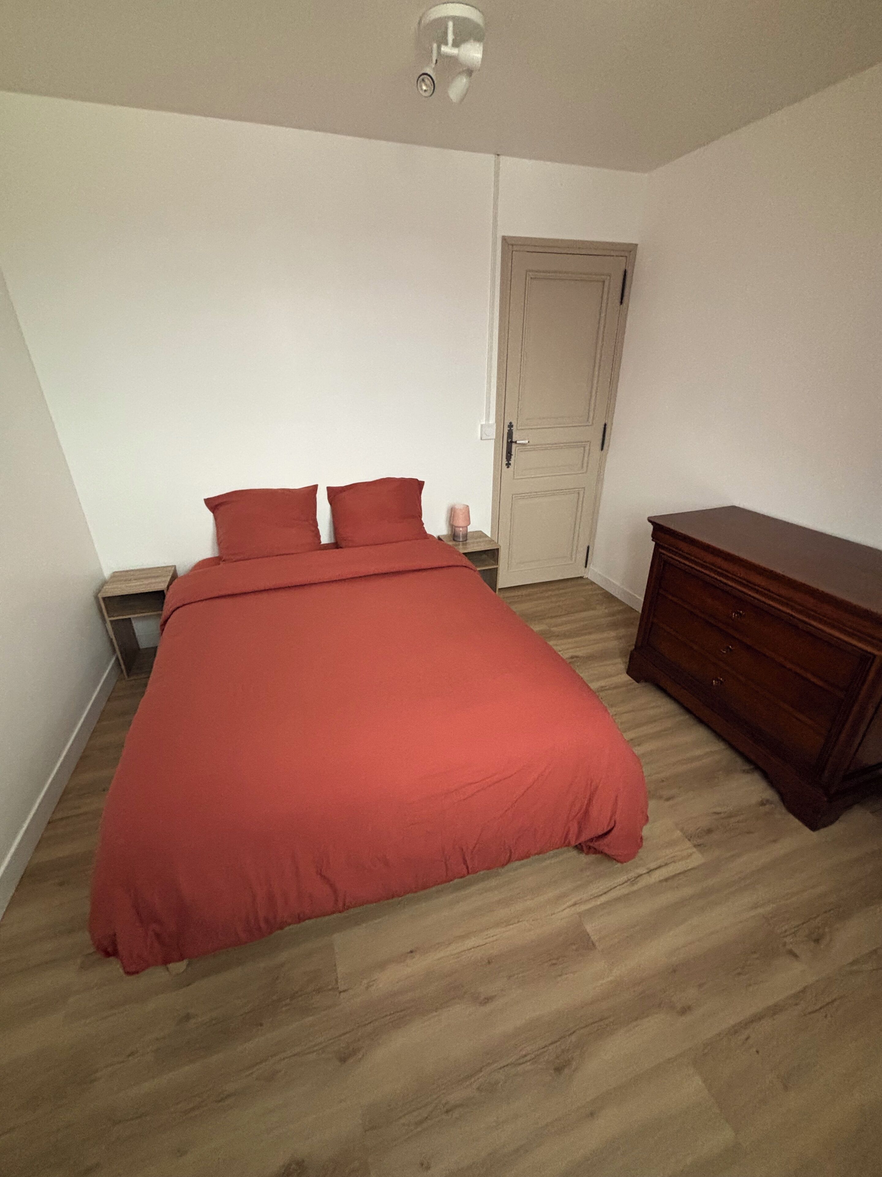 Une chambre à coucher avec un lit, une table de chevet, une commode et une porte.