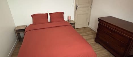 A bedroom with a bed, a nightstand, a dresser, and a door.