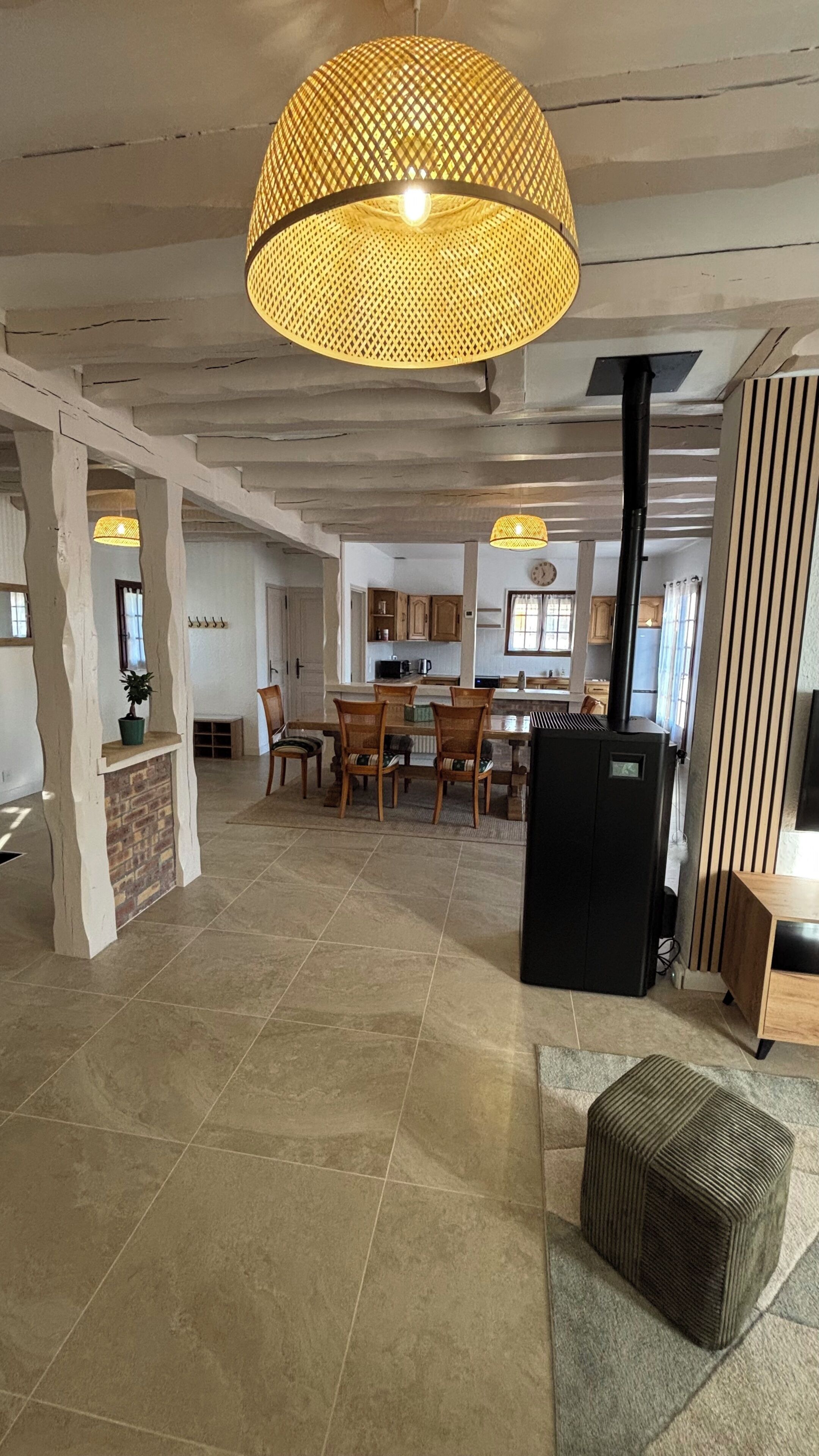 A spacious living area with a dining table, chairs, a black refrigerator, and a large woven light fixture.