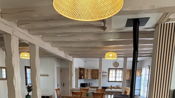 A spacious living area with a dining table, chairs, a black refrigerator, and a large woven light fixture.