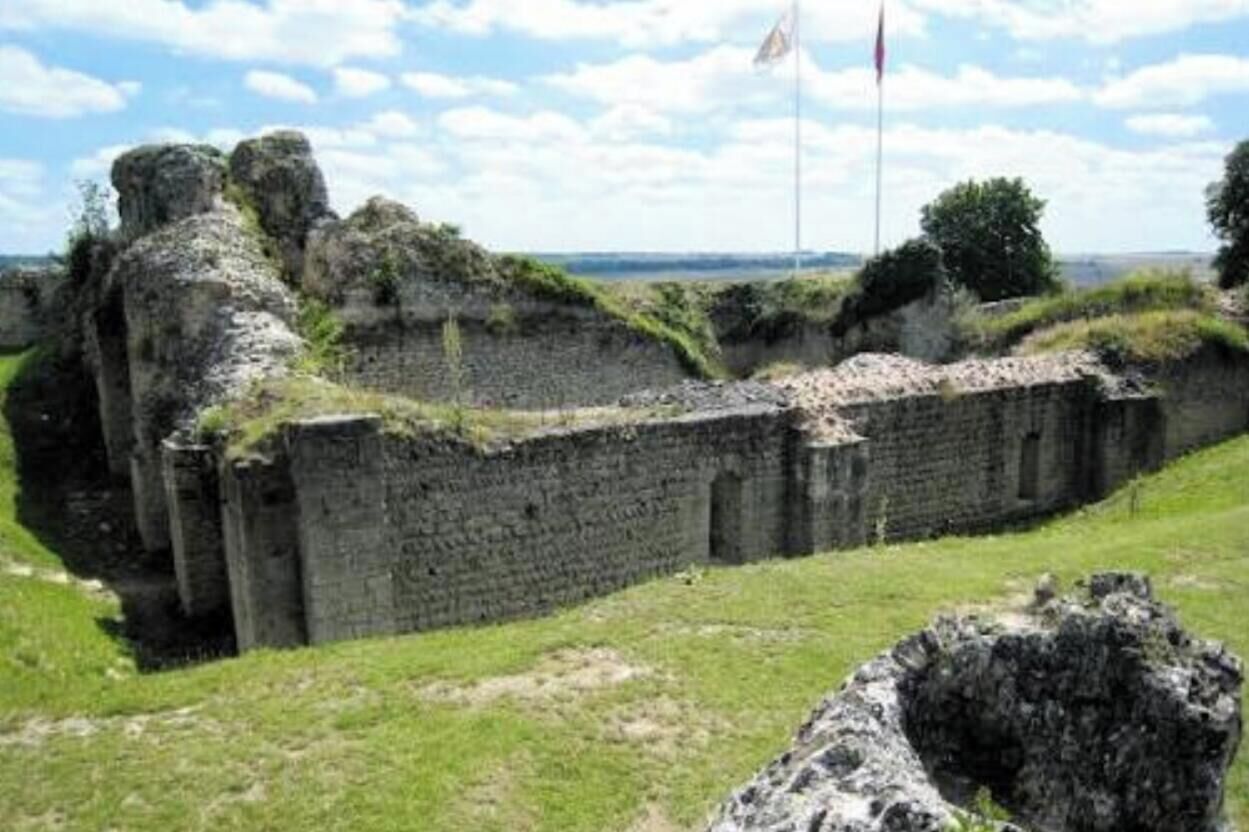 Un mur de pierre ancien, avec une pelouse au premier plan et un mât de drapeau en arrière-plan.