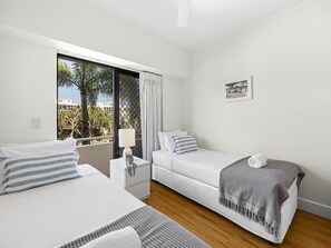Ein Schlafzimmer mit zwei Betten, einem Fenster mit Vorhängen, einem Nachttisch und einem Wandbild.