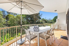 Een balkon met een tafel, stoelen, een parasol en uitzicht op groen.