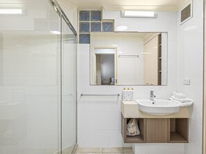 Et moderne badeværelse med brusekabine i glas, et stort spejl og en vask med toiletartikler.