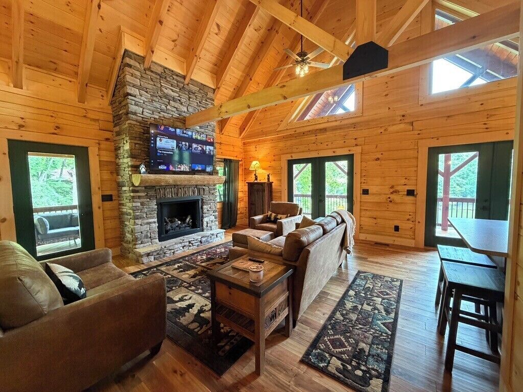 A log cabin interior with a stone fireplace, leather sofa, and a dining table.