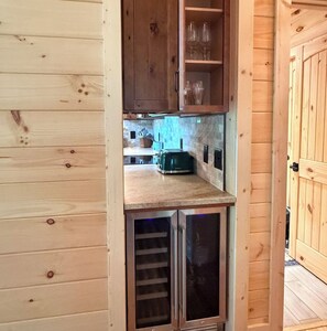 Interior de madera con cocina integrada, que incluye un tostador y un armario con copas de vino.