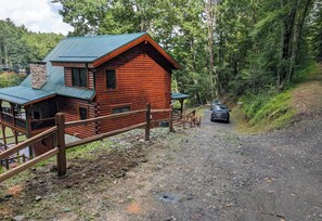 A log cabin with a green roof, a wooden deck, and a gravel driveway. - Log Cabin on the Lake with Private Dock-Hot Tub-Fireplace-Arcade-Close to town! (West Jefferson)