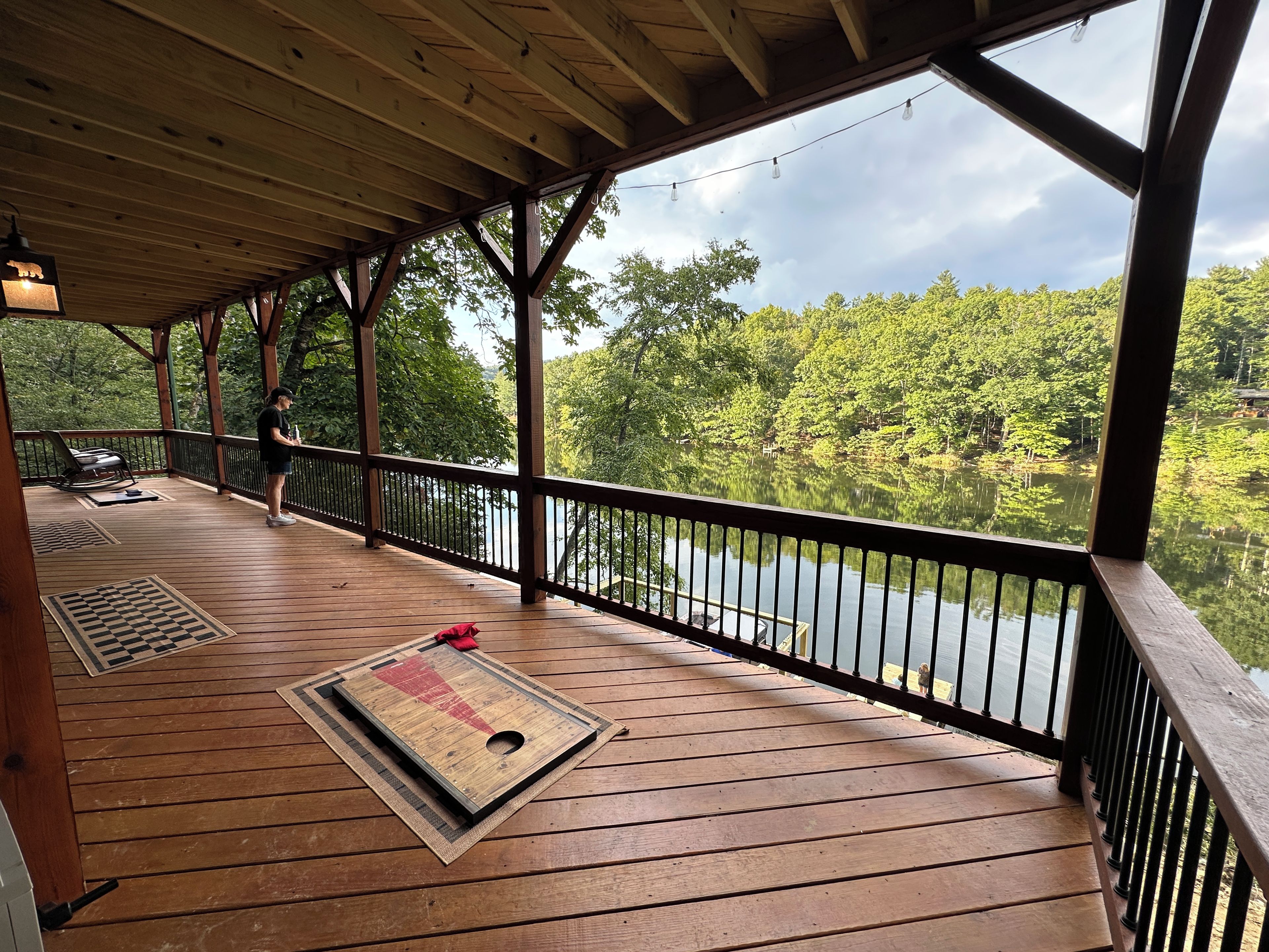 A wooden deck with a railing overlooking a lake, a bench, and a mat on the floor.